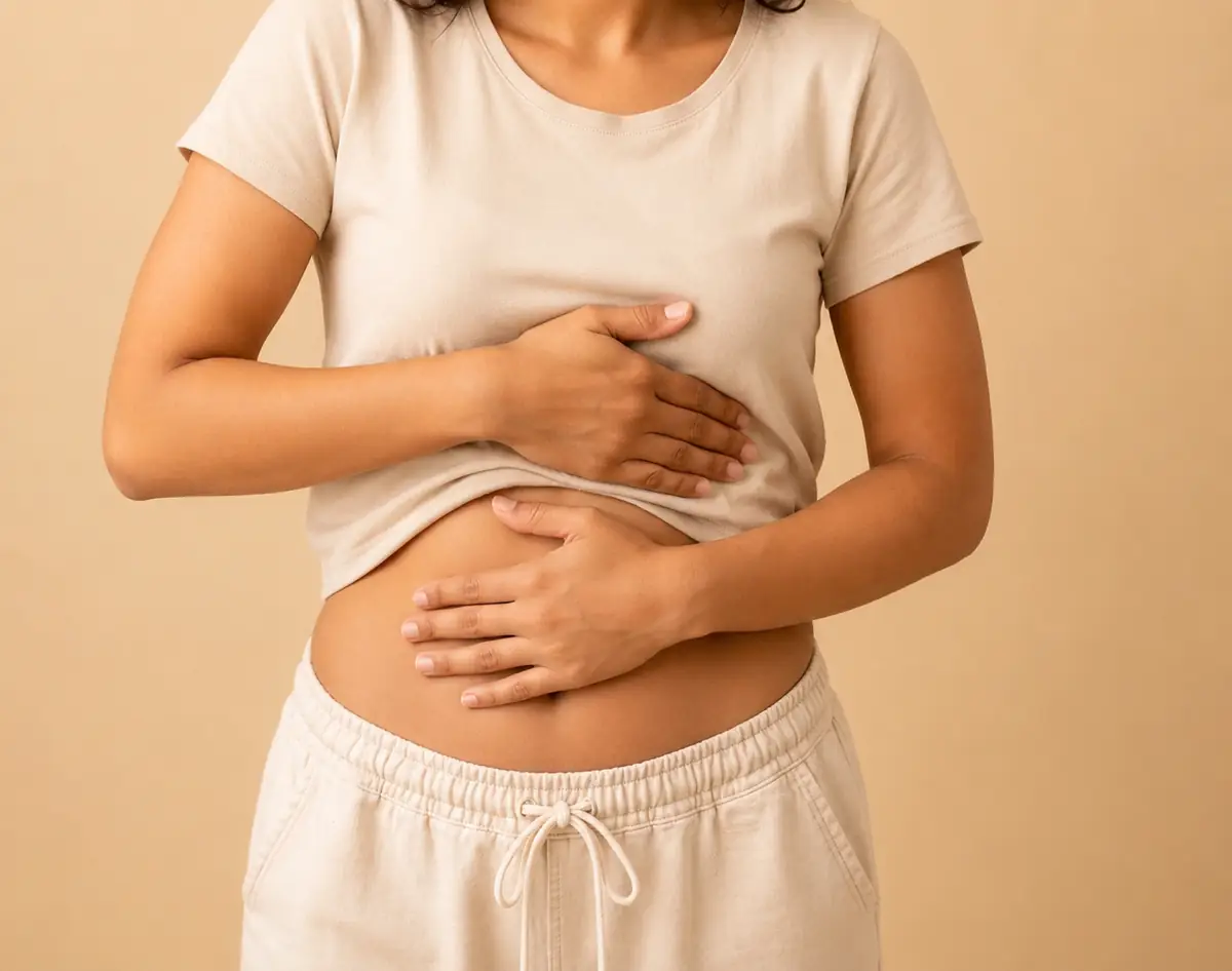Mulher com a mão na barriga sentindo desconforto abdominal.
